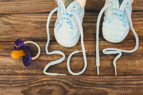 2017 new year written laces of children\'s shoes and pacifier on old wooden background. Toned image