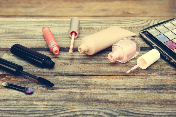 Cosmetics: mascara, concealer, nail polish, perfume, lip gloss and eye shadow on wooden background. Toned image.