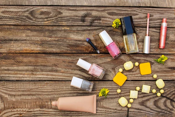 Cosmetics:, false eyelashes, concealer, nail polish, perfume, lip gloss, beads, and yellow flowers on wooden background. Toned image.