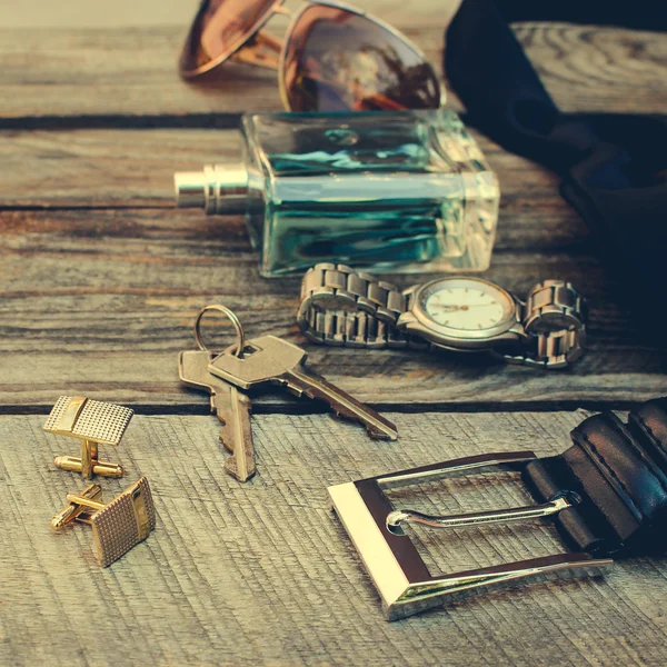 Men accessories: sunglasses, wrist watch, cufflinks, strap, keys, tie, perfume on old wood background. Toned image.