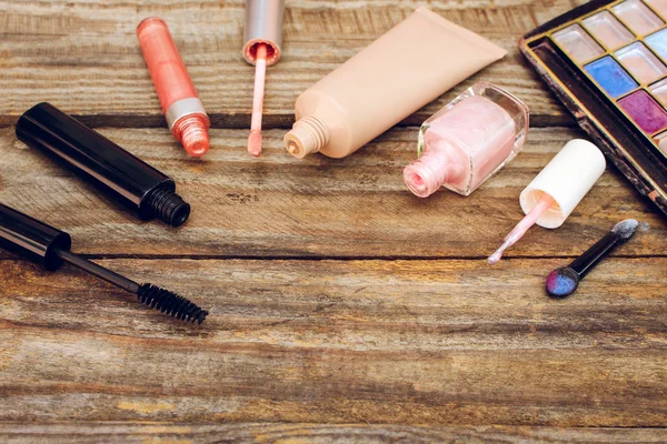 Cosmetics: mascara, concealer, nail polish, perfume, lip gloss and eye shadow on old wooden background. Toned image.