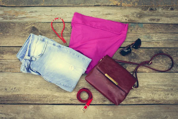 Summer women\'s clothing: t-shirt, beads, handbag, jeans on old wooden background. Toned image.