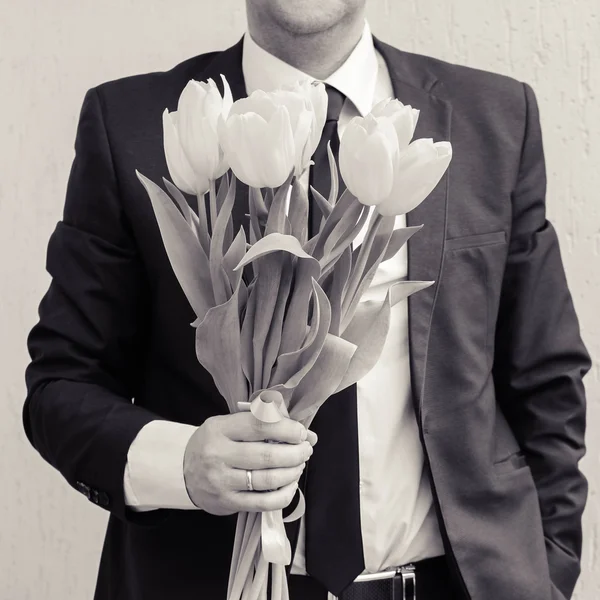 A man wearing a business suit, holding a bouquet of tulips. The man gives a bouquet of flowers. Black and white shot.