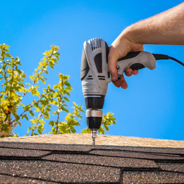 The man puts a soft roof on a house roof. The construction of houses, roofs. Builder twists the screwdriver the screws in the roof.