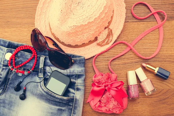 Summer women\'s accessories: sunglasses, beads, denim shorts, mobile phone, headphones, a sun hat, handbag, lipstick, nail polish. Toned image