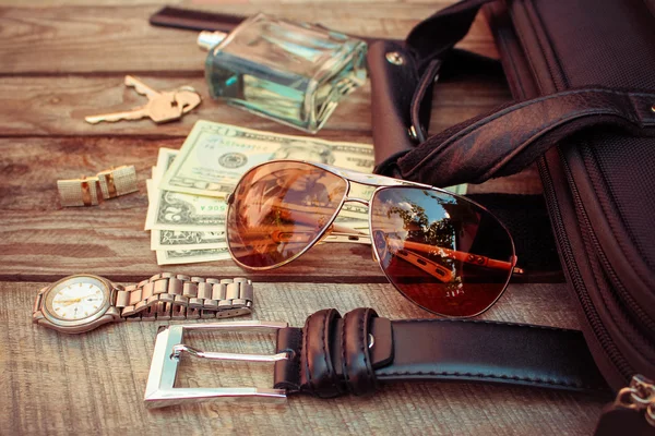 Men accessories: sunglasses, bag, money, wrist watch, cufflinks, comb, strap, keys, perfume on the old wood background. Toned image.