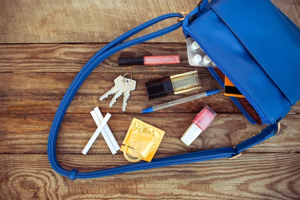 Things from open lady handbag. Cosmetics, female accessories, birth control pill, cigarette and condom falls out of pocket with handbags on wooden background. Toned image.