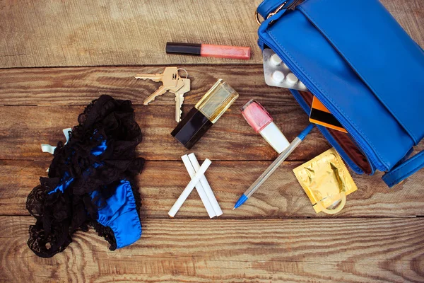 Things from open lady handbag. Cigarette, condom, panties, credit card, keys and cosmetics falls out of pocket with handbags on wooden background. Toned image.