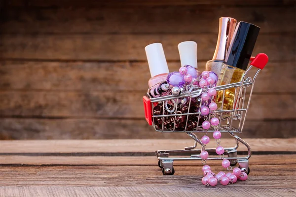 Shopping cart with cosmetics, beads, hair clip on the old wood background. Toned image.