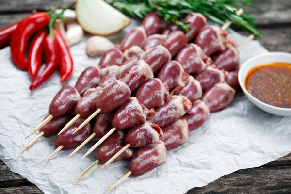 Ready to cook Duck Heart stringed on skewers BBQ with hot sauce and chili pepper. decorated with greens and vegetables. background