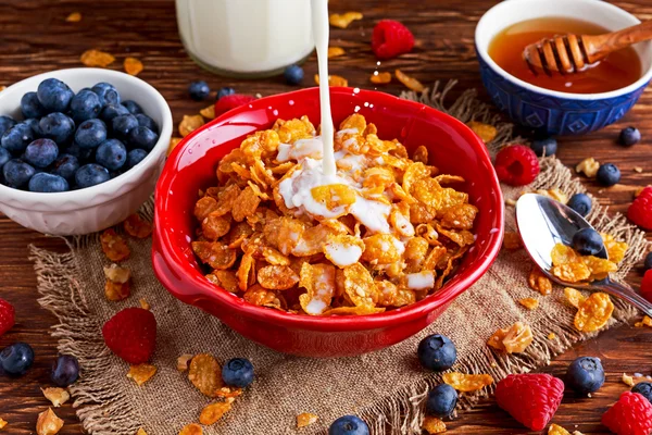 Corn Flakes with berries raspberries, blueberries, pouring milk, and sweet honey.