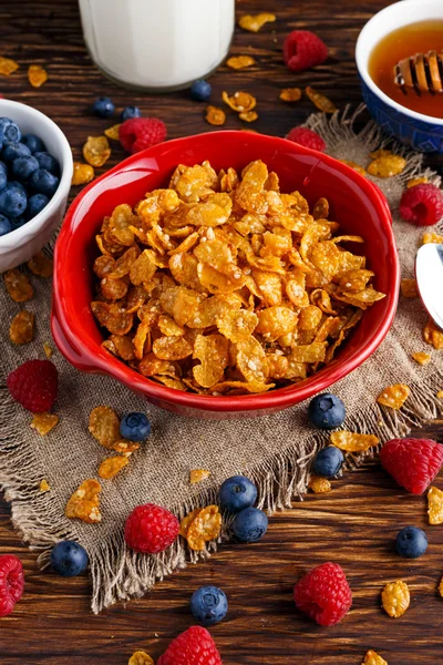 Corn Flakes with berries raspberries, blueberries, glass of milk, and sweet honey.