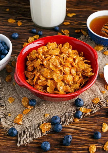 Corn Flakes with berries raspberries, blueberries, glass of milk, and sweet honey.