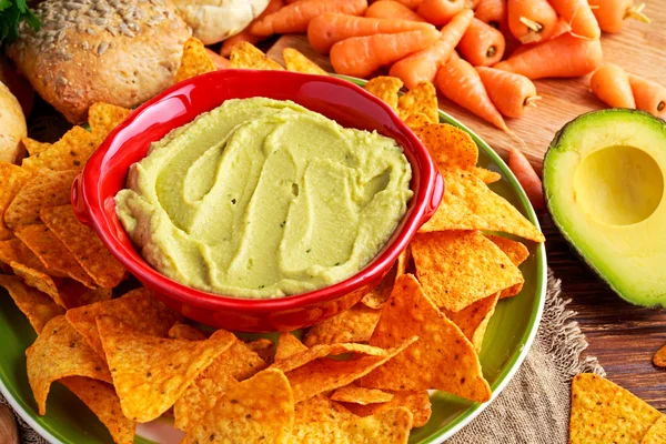 Classic Homemade avocado hummus with olive oil, carrots, pita chips, lime, chilli, parsley.
