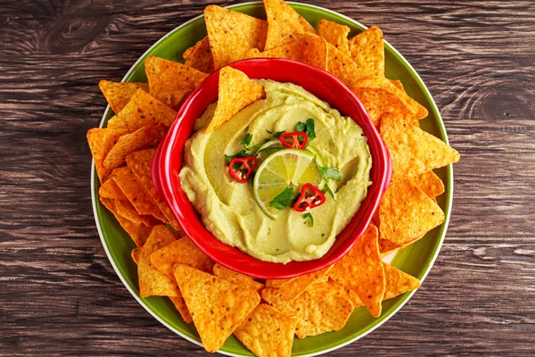 Classic Homemade avocado hummus with olive oil, pita chips, lime, chilli, parsley on wooden background