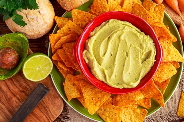 Classic Homemade avocado hummus with olive oil, carrots, pita chips, lime, chilli, parsley.