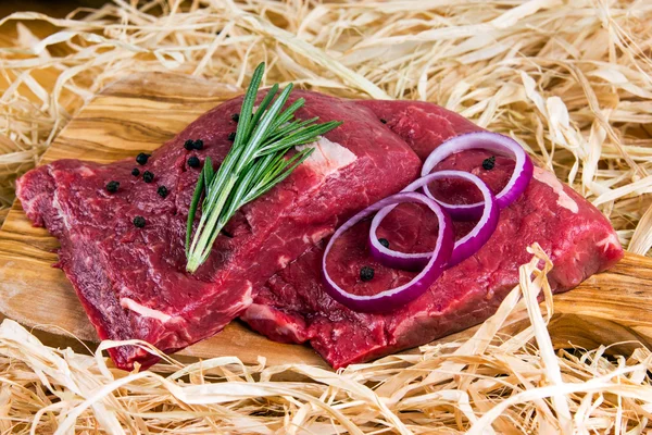 British Beef Flat Iron steak on cutting board and straw, rosemary and onion