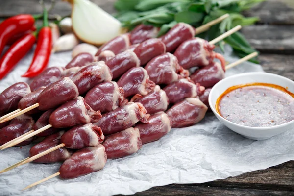 Ready to cook Duck Heart stringed on skewers BBQ with hot sauce and chili pepper. decorated with greens and vegetables.  background.