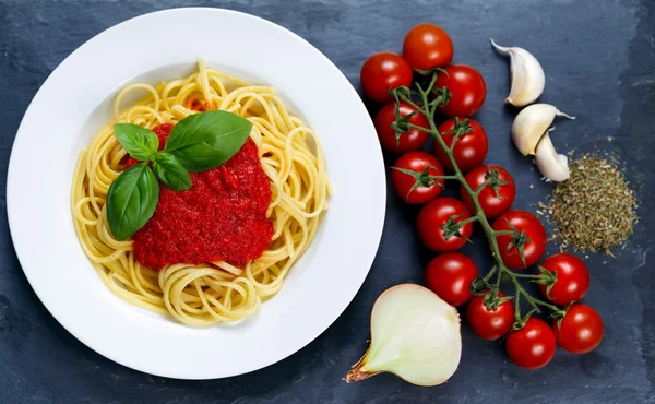 Spaghetti with marinara sauce and basil leaves on top, decorated with cherry tomatoes, garlic, onion, Italian herbs mix  on blue background