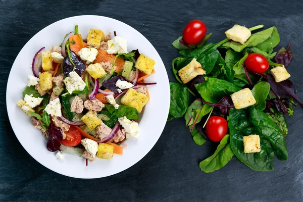 Tuna salad with Spinach, rocket, red ruby chard, tomatoes, cucumbers, white cheese, carrot, red onion, croutons on old blue stone background