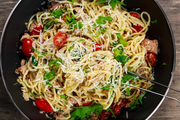 Italian Tuna Pasta spaghetti in wok, with tomato, chilli, parmesan and wild rocket  lives. on old wooden table