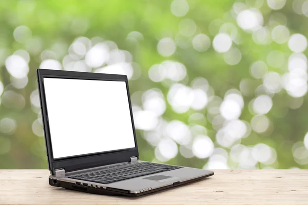Laptop with blank screen on wooden table with nature bokeh backg