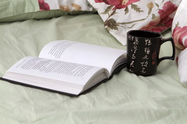 Black mug with a black book on the bed linens flowered