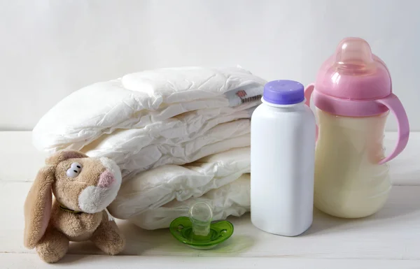 New born child stack of diapers, nipple soother, bunny toy and baby feeding bottle