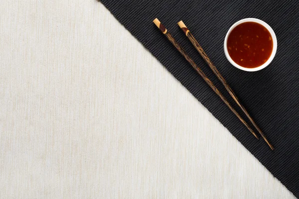 Chopsticks and bowl with sauce on table mat top view