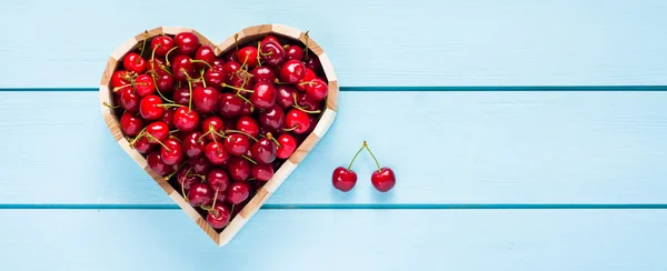 Cherries in a heart box on blue wooden table top view