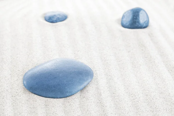 Three blue stones on white sand