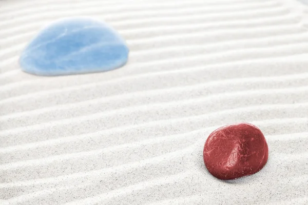 Red and blue stones on white sand, shallow depth of field