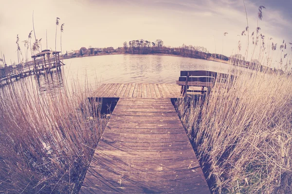 Vintage toned fisheye lens image of a wooden pier on lake.