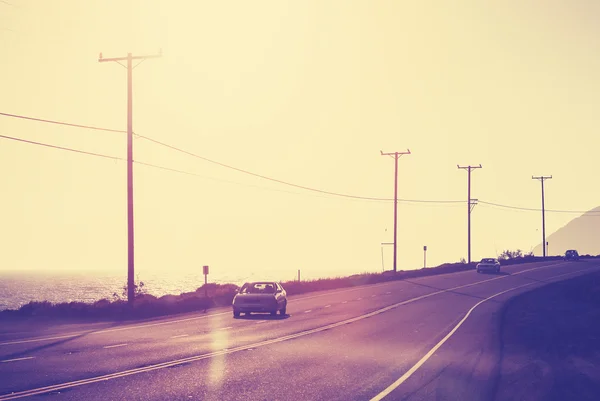 Vintage toned ocean road against sun with flare effect.