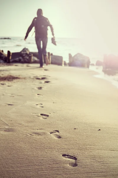 Footprints on beach, woman out of focus, retro effect.