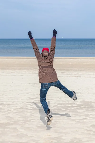 Woman jumping on beach, winter active lifestyle concept.