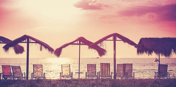 Retro filtered picture of beach chairs and umbrellas at sunset.