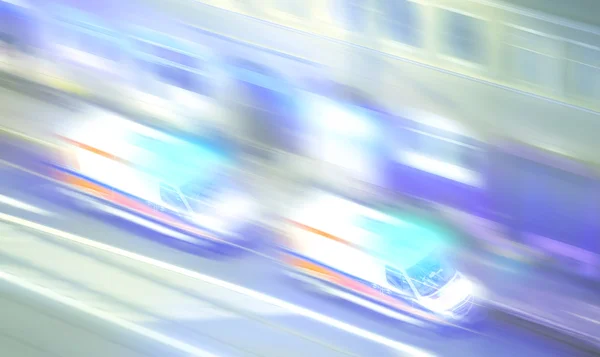Motion blurred ambulances with flashing lights at night.