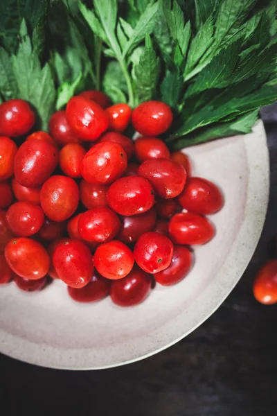 Small tomatoes and green vegetable on rustic black wooden backgr