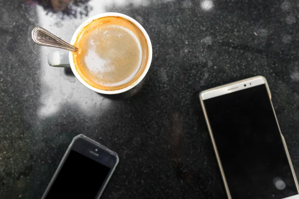 Digital smartphone and cup of coffee on desk with vintage flower