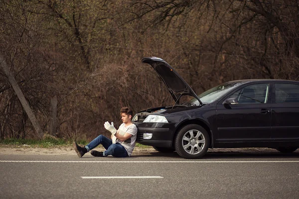 Upset man checking his car engine after breaking down