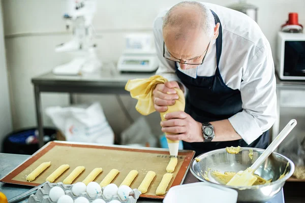 Baker prepares a cake and eclairs