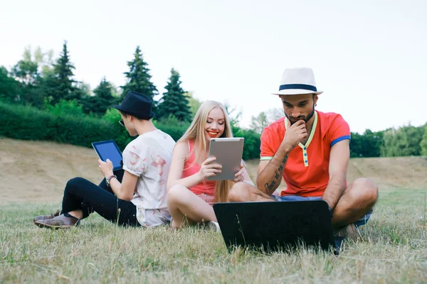 Technology and people concept - group  friends with tablet pc computers , smartphone sitting  in park