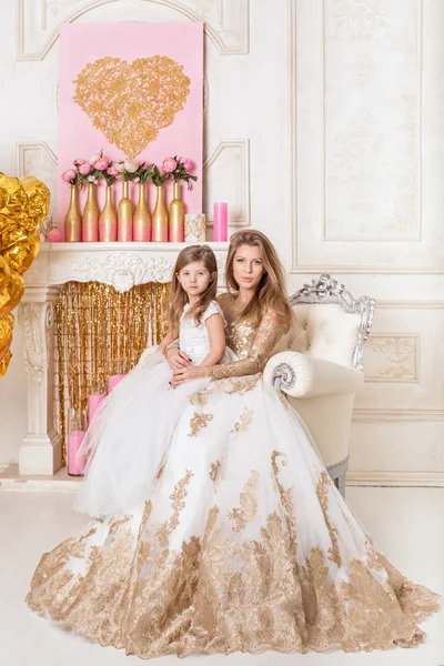 Mother and daughter in beautiful white evening gown, sitting in a chair.
