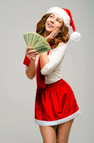 Girl in a suit and Santa hat. Keep money and looking up excitedly.Smiling happy girl on grey background.
