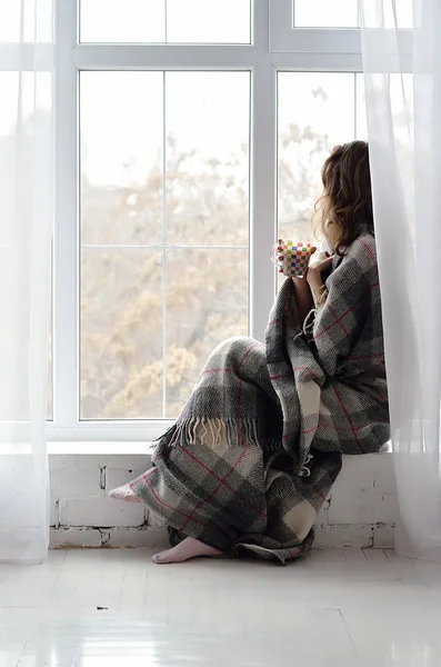 Young woman drinking tea sitting on the windowsill.