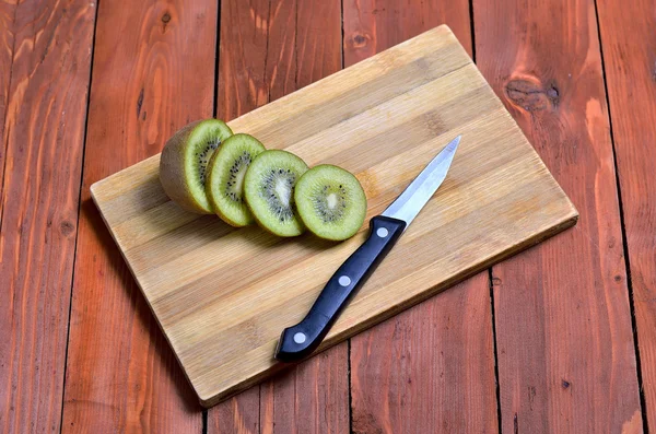 Slices of fresh kiwi fruit and a knife on a wooden background.