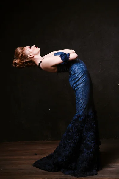 Studio shoot of posing woman in long blue dress. Retro style.