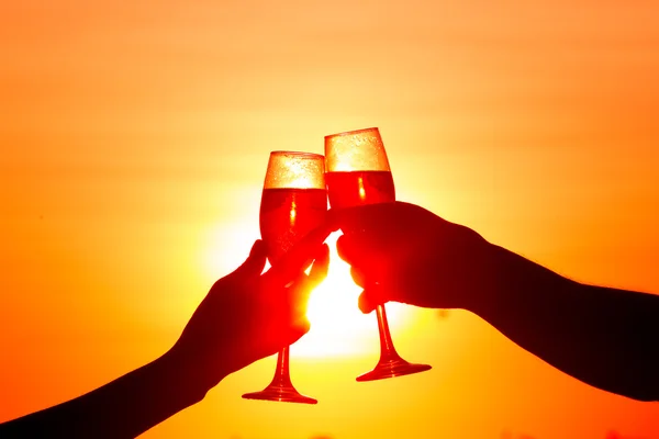 Man and woman clanging wine glasses with champagne at sunset