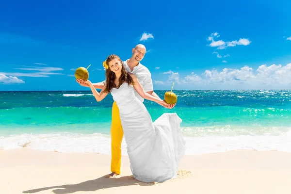 Happy bride and groom drink coconut water on a tropical beach. W